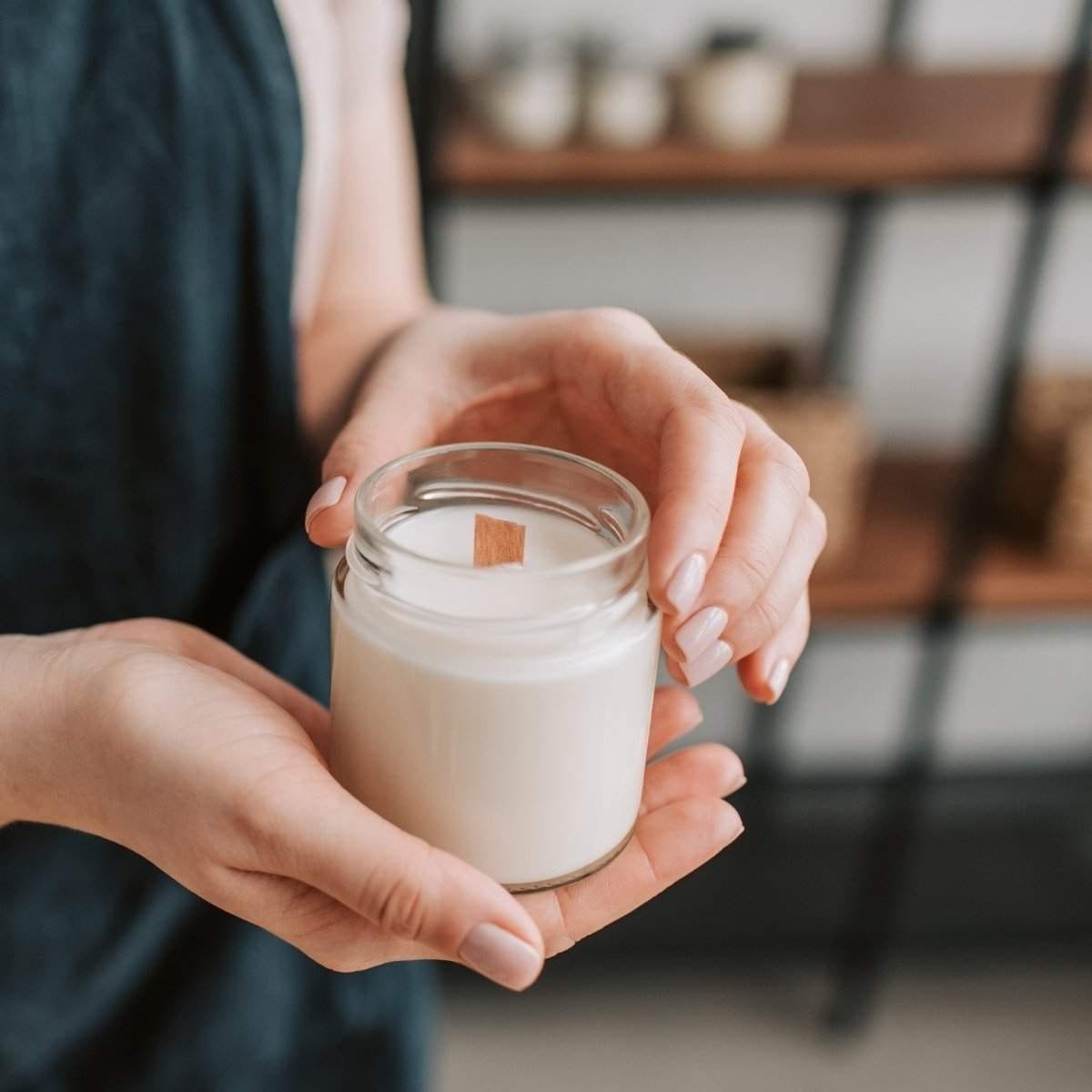 Une créatrice de Niõ tient une nouvelle bougie parfumée artisanale en cire végétale et mèche en bois dans son pot en verre transparente de qualité