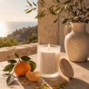 La scène au bord d'une fenêtre d'une maison d'un village en Sicile, une mandarine et une bougie parfumée de Niõ posées, avec la vue mer derrière