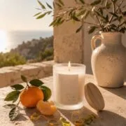 La scène au bord d'une fenêtre d'une maison d'un village en Sicile, une mandarine et une bougie parfumée de Niõ posées, avec la vue mer derrière