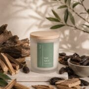 Bougie Bois Sacré de Niõ, parfumée au Santal, dans un décor épuré entouré des écorce de bois de santal de fèves de tonka