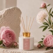 Diffuseur de parfum Pivoine Sauvage de Niõ posé sur un socle en pierre naturelle et entouré des pivoines fraiches