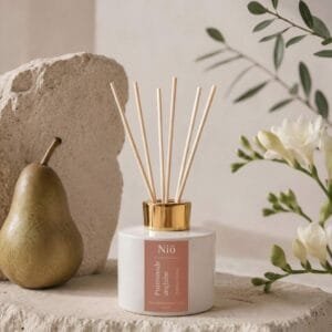Diffuseur de parfum Promenade Anglaise, posé avec une poire et un brin de Freesia sur un socle en pierre naturelle dans un décor épuré et raffiné