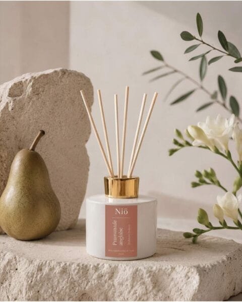 Diffuseur de parfum Promenade Anglaise, posé avec une poire et un brin de Freesia sur un socle en pierre naturelle dans un décor épuré et raffiné