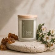 Bougie Velours Ambré de Niõ dans un cadre épuré, posée sur une pierre naturelle comme socle entre les résidus de l'ambre et des fleurs de jasmin