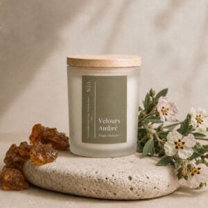 Bougie Velours Ambré de Niõ dans un cadre épuré, posée sur une pierre naturelle comme socle entre les résidus de l'ambre et des fleurs de jasmin