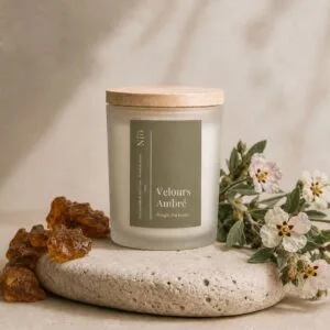 Bougie Velours Ambré de Niõ dans un cadre épuré, posée sur une pierre naturelle comme socle entre les résidus de l'ambre et des fleurs de jasmin