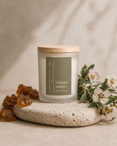 Bougie Velours Ambré de Niõ dans un cadre épuré, posée sur une pierre naturelle comme socle entre les résidus de l'ambre et des fleurs de jasmin