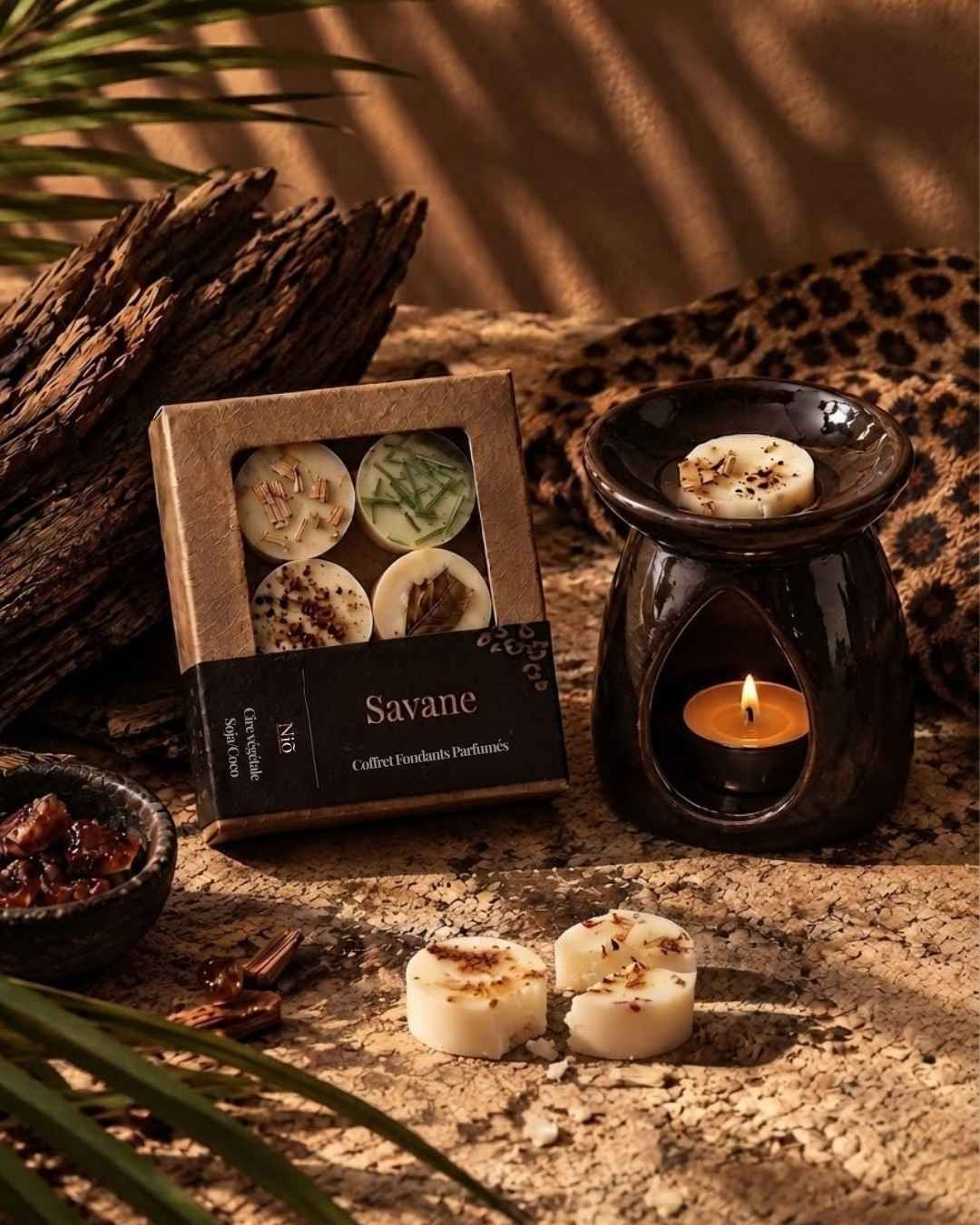 Un fondant Savane en train de fondre sur un brûle-parfum noir allumé, à côté du coffret et de galets de cire.