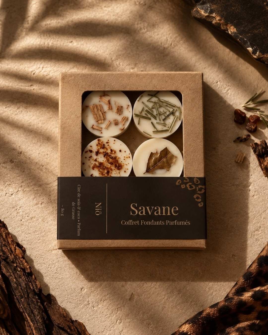 Coffret kraft de quatre fondants parfumés Savane vu de dessus, sur un fond sable avec une étoffe léopard.