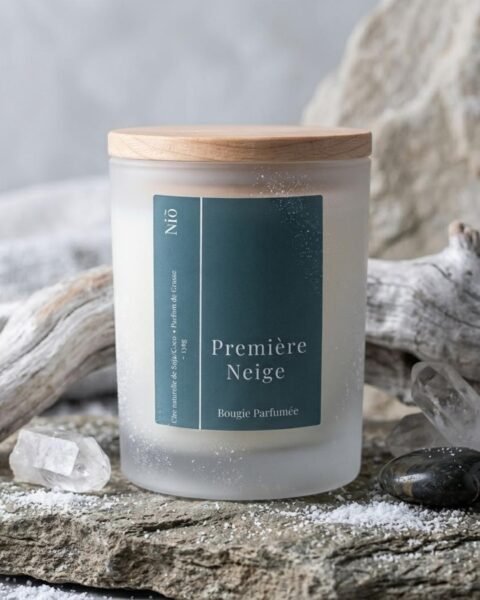 Bougie parfumée Première Neige de la Collection Nuit Polaire, hiver 2026/2027, signée Niõ, dans une ambiance hivernale, sur un socle en pierre naturelle, entourée de givre et de neige